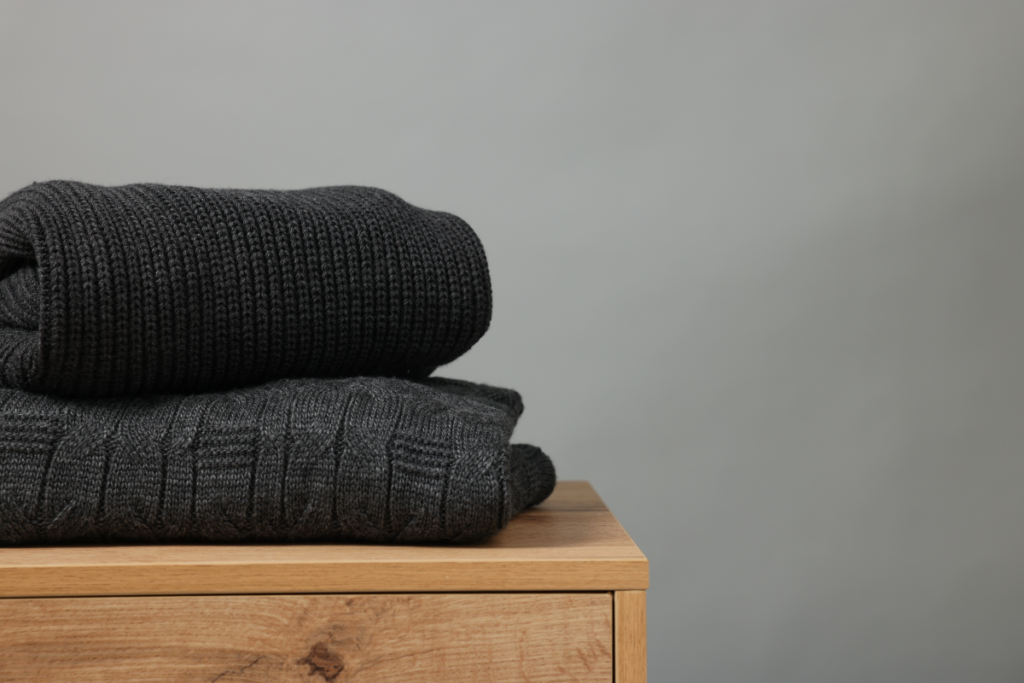 Des vêtements opaques posés sur un meuble en bois